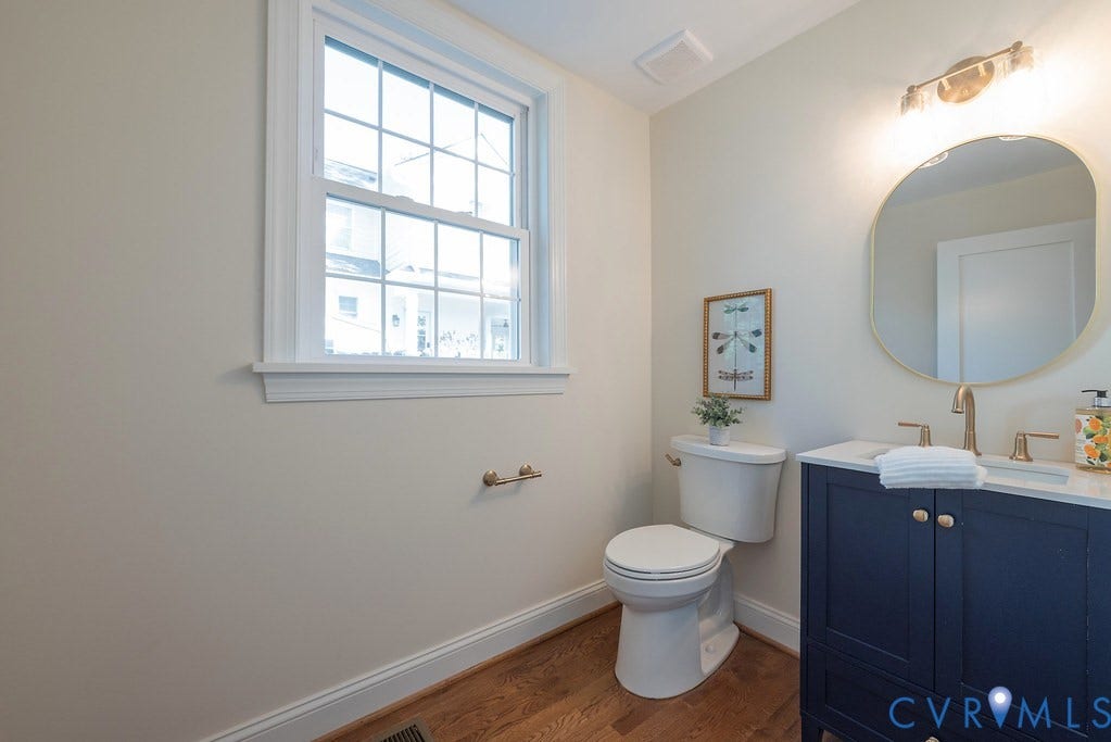 Navy blue vanity with light-toned countertop, oval-shaped wall mirror, wood-finish flooring, and metal finish hardware