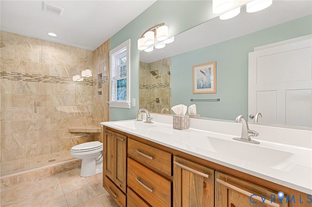 3820 Upshaw Road, Decker's Pond, Aylett, VA 23009 Dual-sink vanity with a solid-surface countertop, walk-in shower with stone tile surround and built-in bench, full-width mirror, and recessed lighting