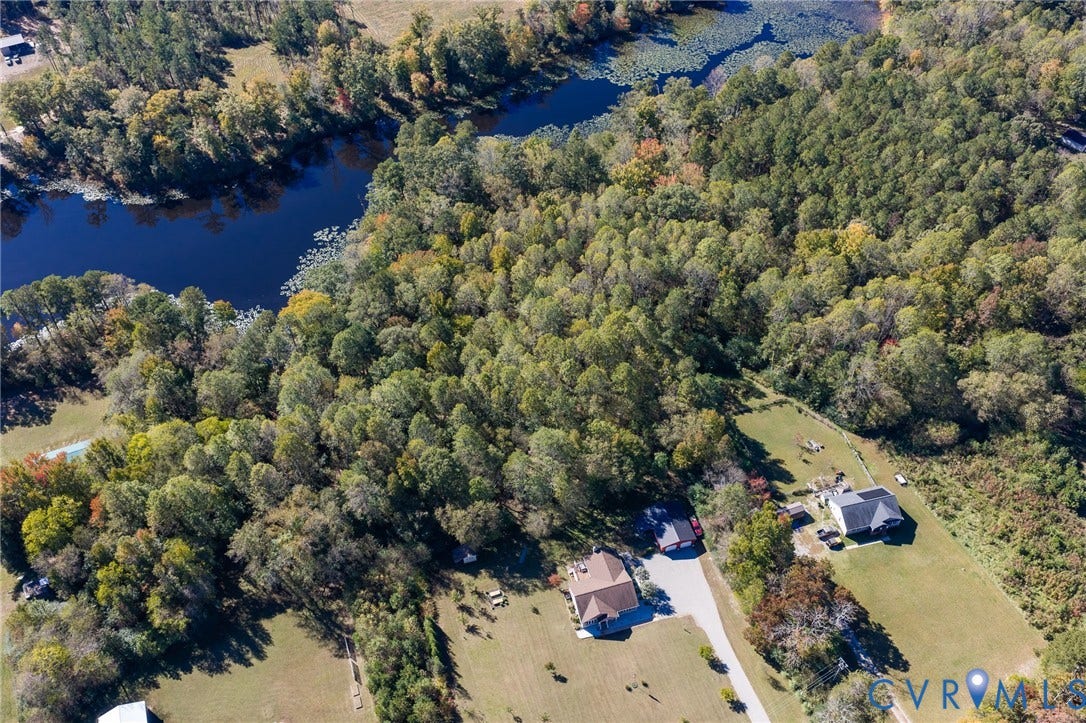 3820 Upshaw Road, Decker's Pond, Aylett, VA 23009 Aerial perspective of a sprawling property featuring mature forest canopy, direct water frontage, expansive cleared acreage, paved private driveway, and residential structures with shingled roofing