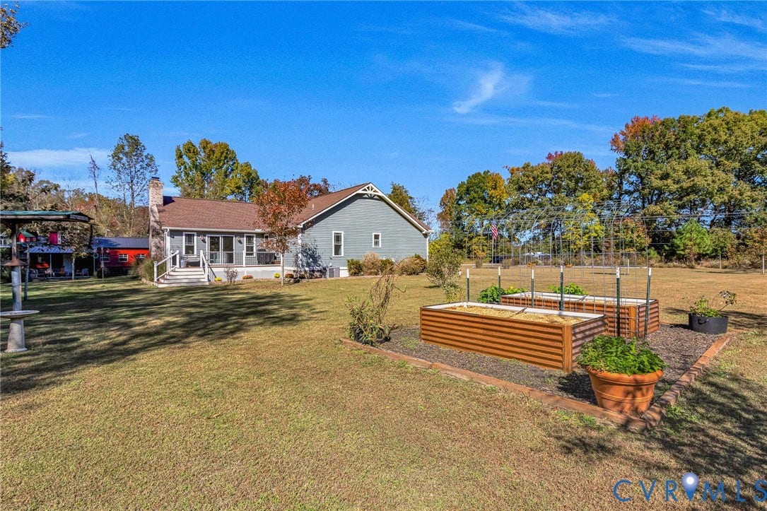 3820 Upshaw Road, Decker's Pond, Aylett, VA 23009 Expansive backyard featuring raised metal garden beds, masonry-bordered landscaping, an attached rear deck with stairs, and exterior horizontal siding
