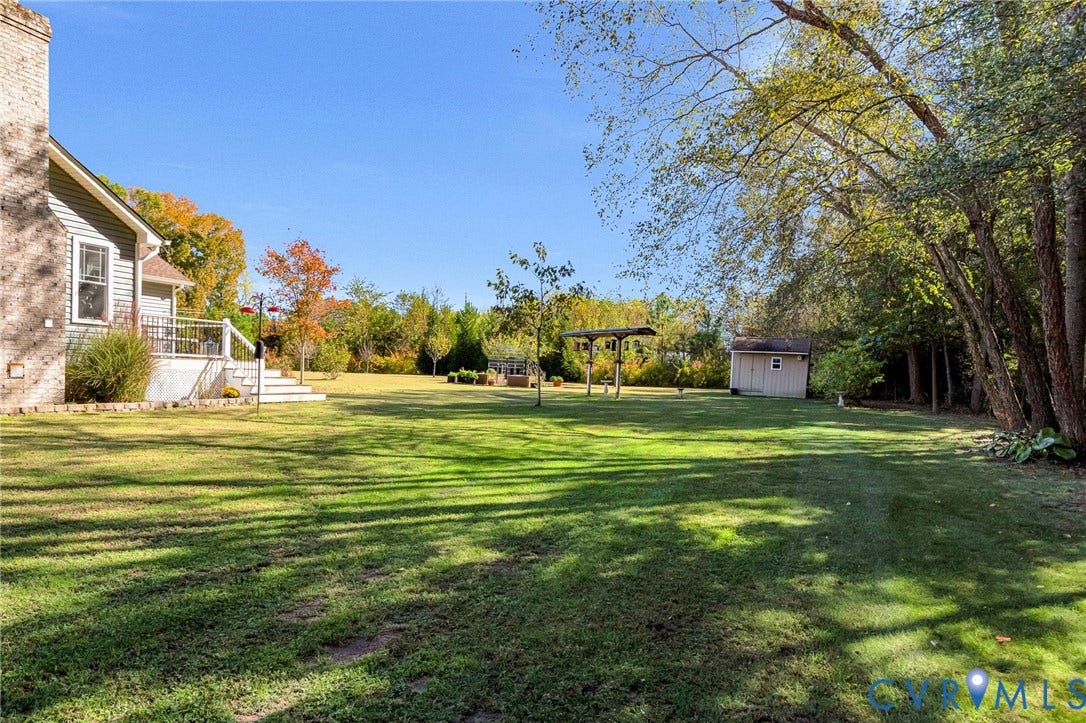 3820 Upshaw Road, Decker's Pond, Aylett, VA 23009 Expansive backyard featuring a brick chimney, raised deck with metal railings, detached storage structure, and mature tree line