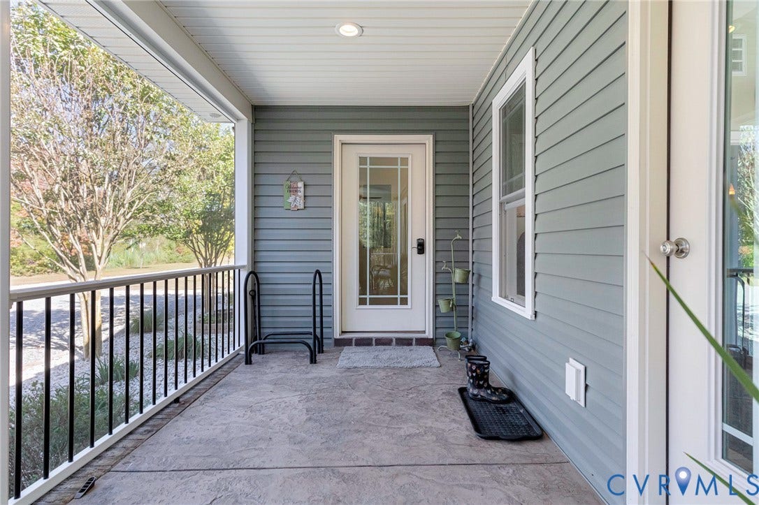 3820 Upshaw Road, Decker's Pond, Aylett, VA 23009 Covered porch featuring textured concrete flooring, horizontal siding, black metal railing, and a glass-paneled entry door