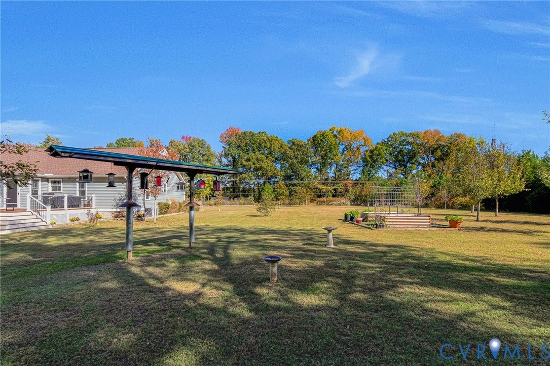 3820 Upshaw Road, Decker's Pond, Aylett, VA 23009 Expansive backyard featuring a large grass lawn, mature trees, a metal trellis structure, and a raised garden bed