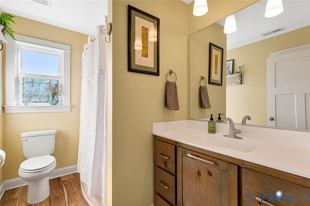 3820 Upshaw Road, Decker's Pond, Aylett, VA 23009 Bathroom featuring a wood-finish vanity with a white countertop, an integrated sink with a metallic faucet, a full-width wall-mounted mirror, and wood-finish flooring