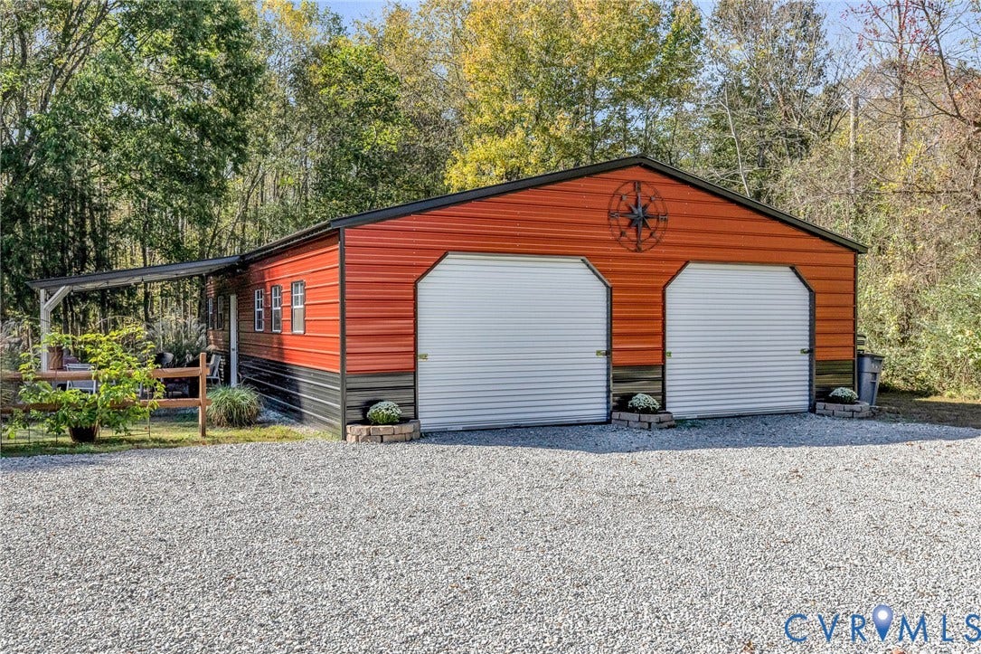 3820 Upshaw Road, Decker's Pond, Aylett, VA 23009 Detached two-car metal garage featuring dual roll-up doors, a side-mounted covered lean-to, and a gravel driveway