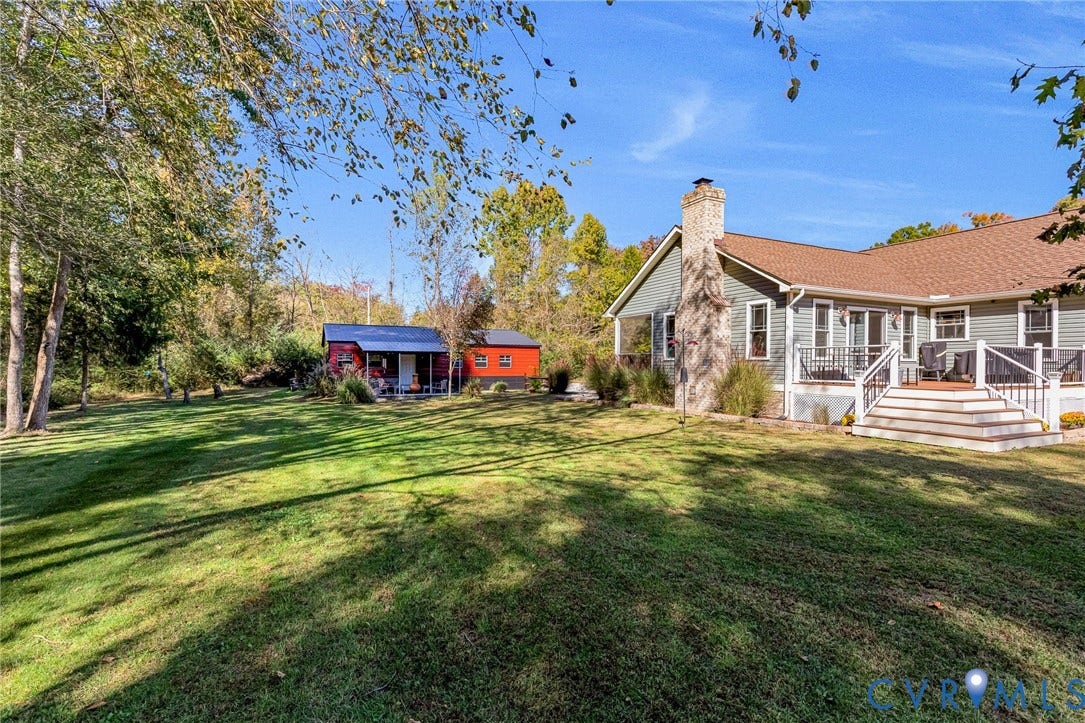 3820 Upshaw Road, Decker's Pond, Aylett, VA 23009 Expansive backyard featuring a manicured lawn, stone-veneer chimney, elevated rear deck with white railing, and detached outbuilding