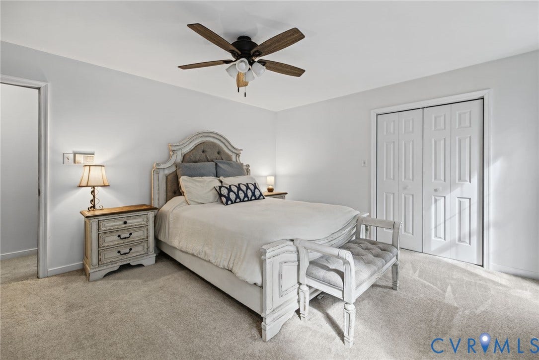 Neutral-toned carpeted room featuring a ceiling fan with integrated lighting and double-door closet cabinetry