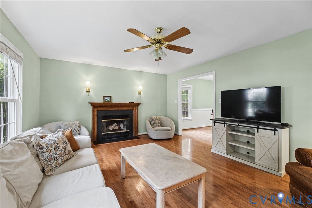 Wood-finish flooring, fireplace with a carved wood mantel, dual wall-mounted sconces, and a ceiling fan with integrated lighting
