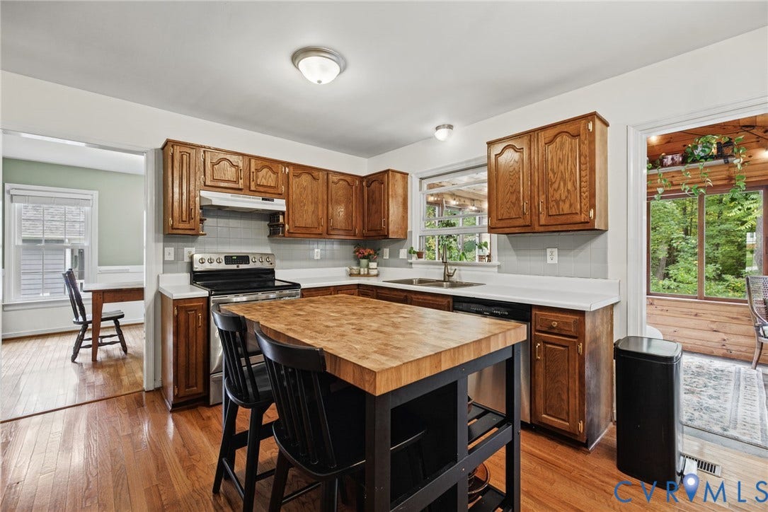 Kitchen featuring wood cabinetry, a butcher-block topped center island, light-toned countertops, tile backsplash, and wood-finish flooring