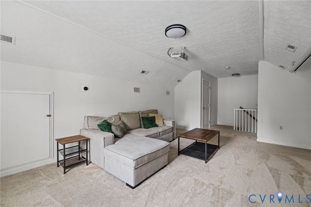 Sloped ceiling interior featuring wall-to-wall carpeting, an integrated ceiling-mounted projector, a recessed storage access panel, and a white balustrade railing
