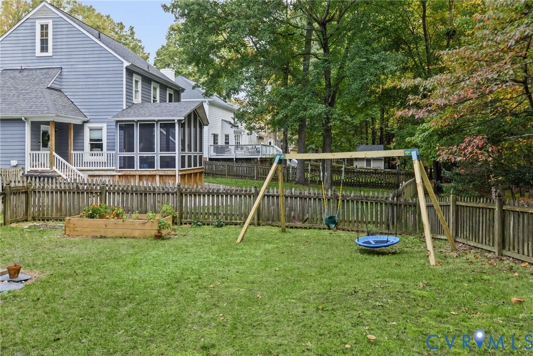 Backyard featuring a wood-slat perimeter fence, screened-in porch, raised garden bed, and mature tree-lined rear grounds