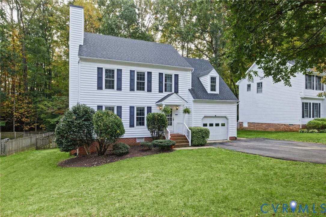 Two-story colonial exterior featuring white horizontal siding, dark shutters, a brick foundation, a front-facing gable roof, and an attached one-car garage
