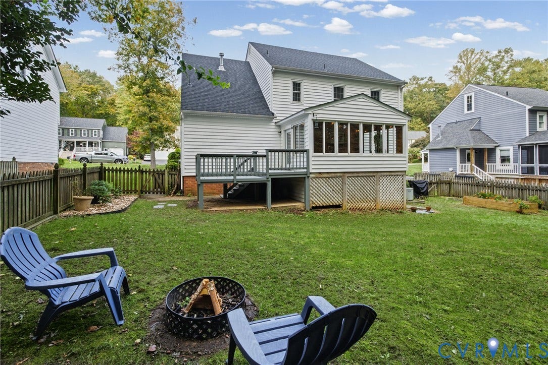 Rear elevation featuring horizontal lap siding, an enclosed sunroom, an elevated wooden deck, and a fenced backyard with a raised garden bed