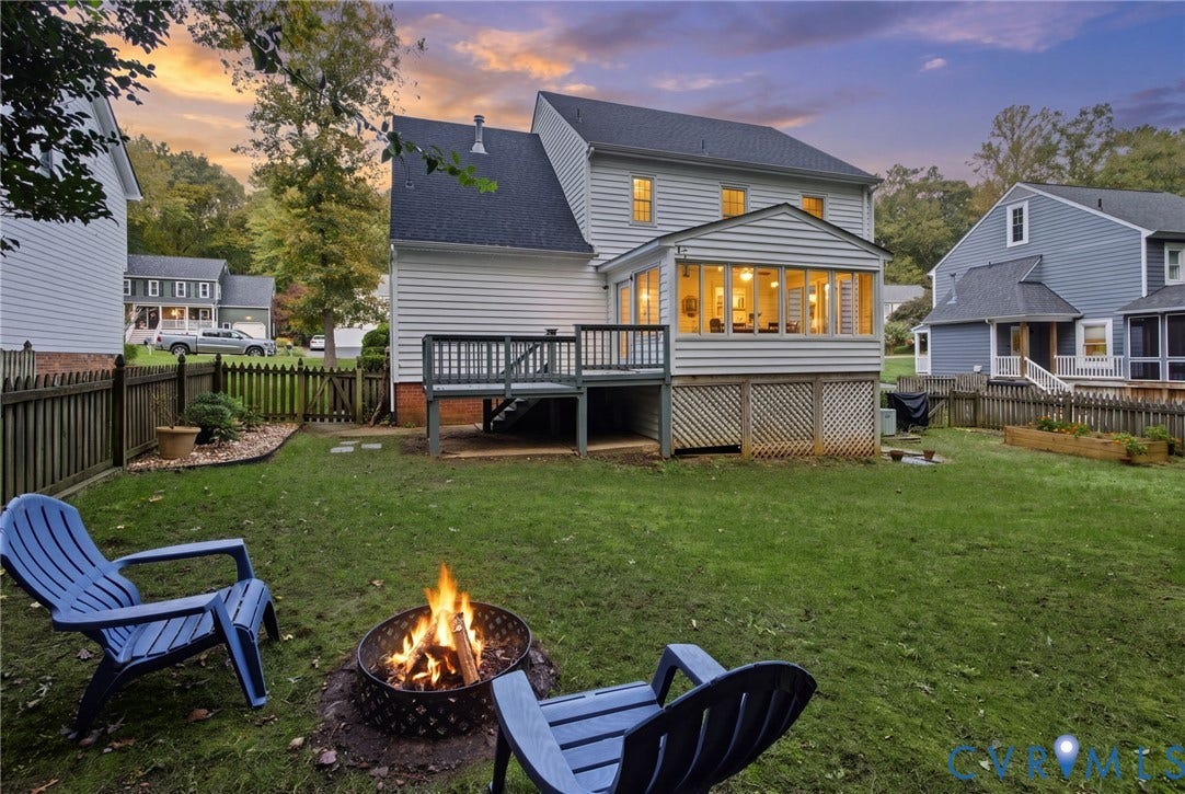 Rear exterior featuring a sunroom, elevated wood deck, lattice skirting, and fenced-in backyard