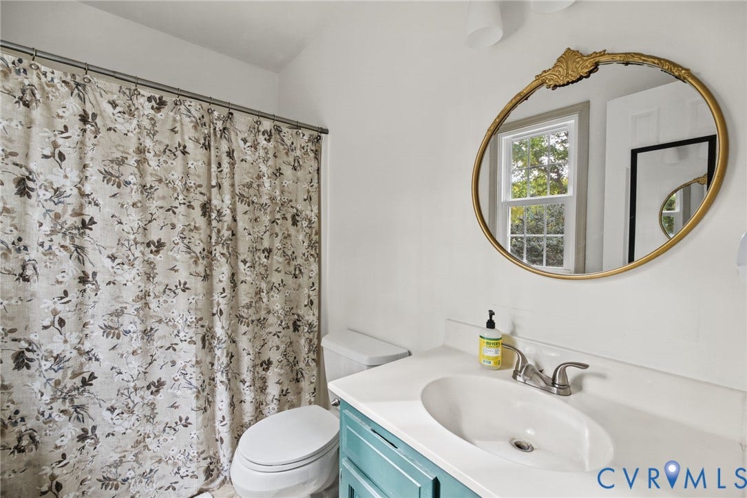 Bathroom featuring a single-basin vanity with a solid-surface countertop, an oval wall-mounted mirror with a decorative gold-tone frame, and a multi-pane window