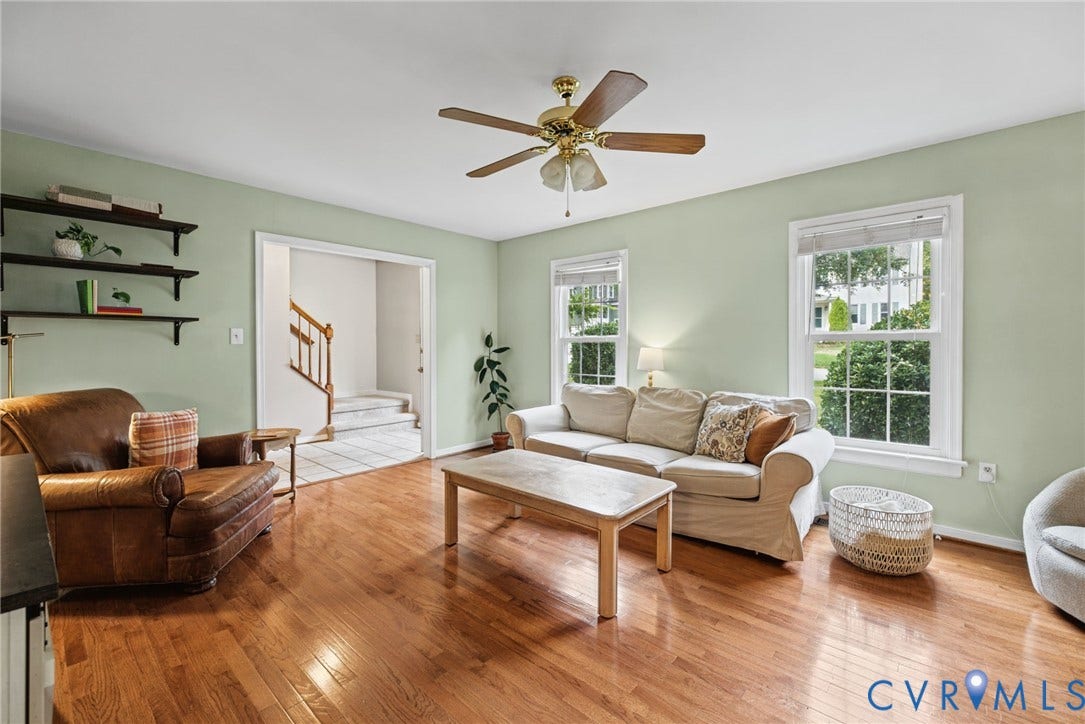 Living space featuring wood-finish flooring, multi-pane windows, wall-mounted shelving, and a ceiling fan
