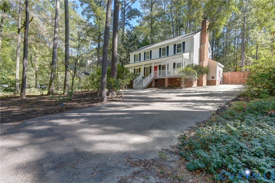 5 Bridgehampton Place, Yorkshire, Henrico, VA 23229 Two-story residence featuring light-colored horizontal siding, a covered front porch with white railing, a side-positioned brick chimney, and a concrete driveway