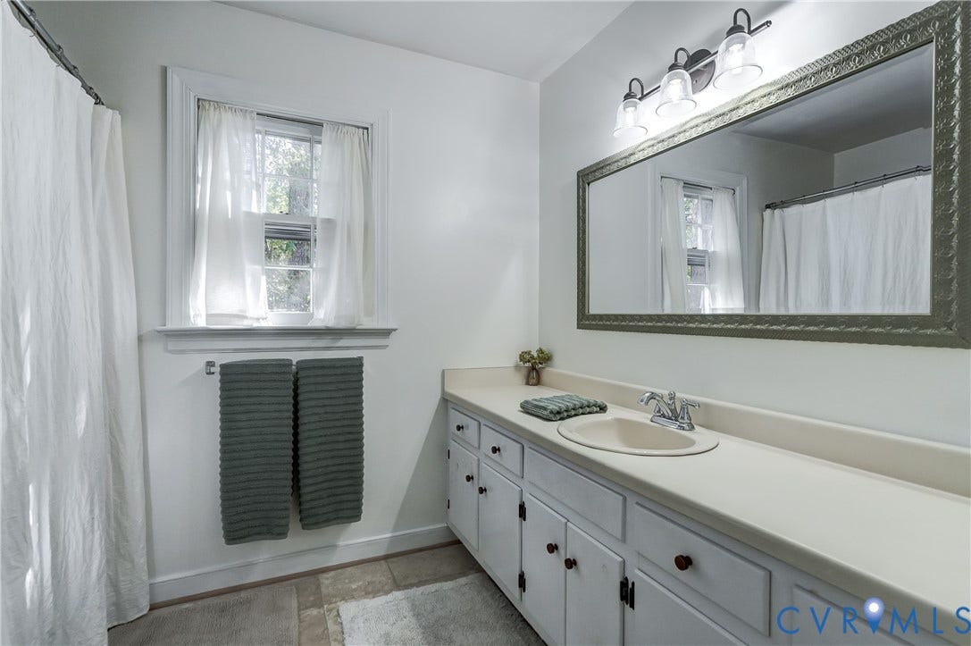 5 Bridgehampton Place, Yorkshire, Henrico, VA 23229 Bathroom featuring a wide white vanity with an integrated basin, a large framed wall-mounted mirror, a three-light fixture, and a window with molded trim
