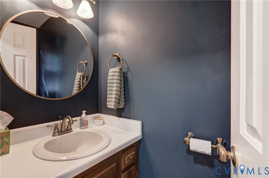 5 Bridgehampton Place, Yorkshire, Henrico, VA 23229 Oval wall mirror with a gold-tone frame, white countertop with an integrated basin, metal hardware, and dual vanity lighting