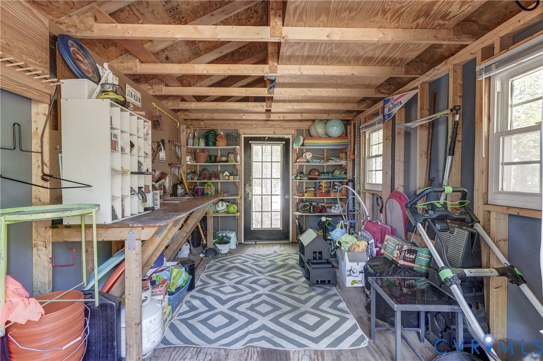 5 Bridgehampton Place, Yorkshire, Henrico, VA 23229 Utility shed with exposed rafter ceiling, built-in wooden workbench, integrated wall shelving, and a glass-paneled exterior door