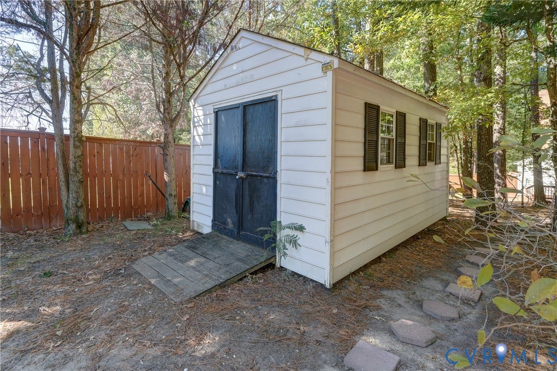 5 Bridgehampton Place, Yorkshire, Henrico, VA 23229 Detached storage structure featuring white horizontal siding, dark shutter-accented windows, double doors with an entry ramp, and a wood-slat perimeter fence