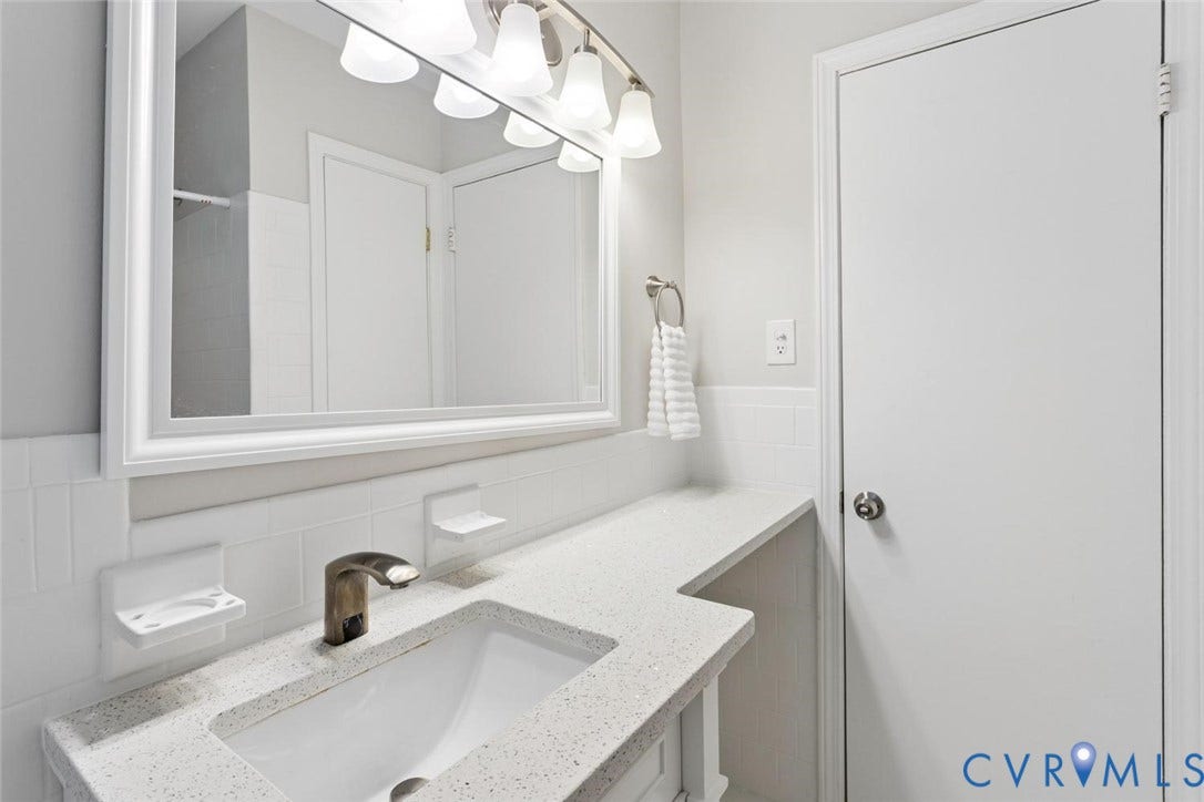 1014 Westbriar Drive, Henrico, VA 23238 Bathroom vanity featuring a quartz-composite countertop, integrated undermount sink, brushed-metal faucet, white subway tile backsplash, and a framed wall mirror with integrated multi-bulb lighting