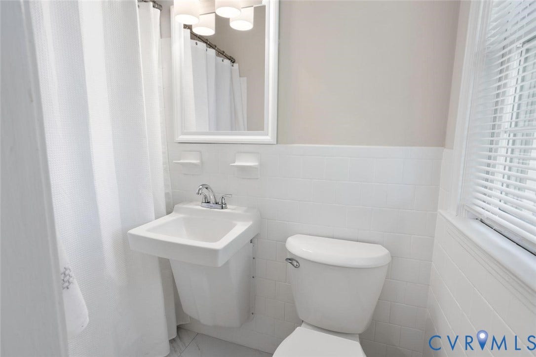 1014 Westbriar Drive, Henrico, VA 23238 Wall-mounted sink with dual-handle chrome faucet, white subway tile wainscoting, recessed medicine cabinet with integrated lighting, and white porcelain toilet