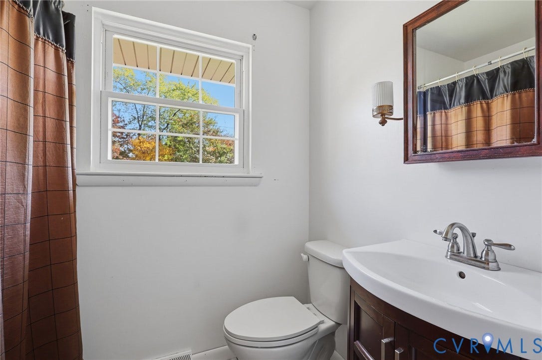 628 Ryan Avenue, Ryan, Colonial Heights, VA 23834 Bathroom featuring a dark-finish vanity with a white integrated sink, polished chrome faucet, wooden-framed mirror, and a double-hung window
