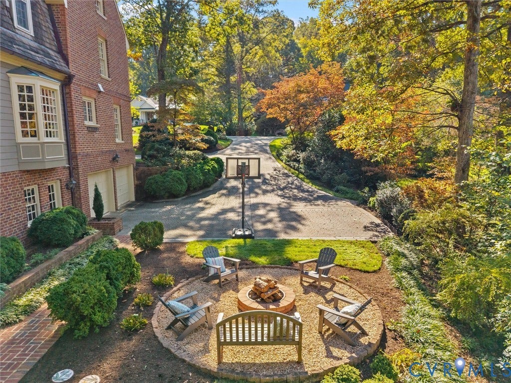 105 Running Cedar Lane, Countryside, Henrico, VA 23229 Brick exterior featuring a circular gravel fire pit, paved driveway, mature trees, and landscaped shrubbery