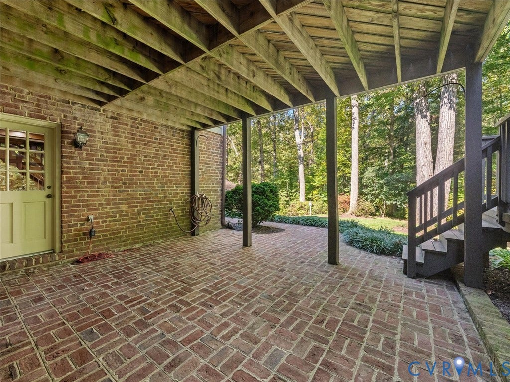 105 Running Cedar Lane, Countryside, Henrico, VA 23229 Covered patio featuring a herringbone-patterned brick floor, exposed timber ceiling joists, brick exterior wall, and an attached staircase with wooden railings