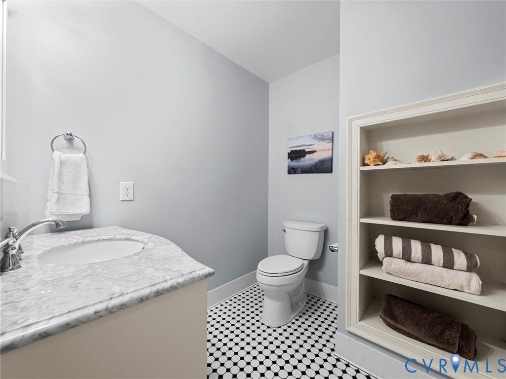 105 Running Cedar Lane, Countryside, Henrico, VA 23229 Vanity featuring a stone countertop and integrated oval sink, complemented by black and white mosaic tile flooring, a wall-mounted ring towel holder, and built-in recessed shelving