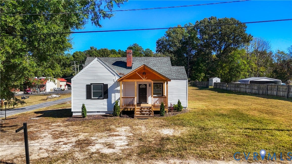 4003 Lee Boulevard, Dinwiddie, VA 23803 White siding exterior with a red brick chimney, covered front porch featuring wood-post supports, and an expansive side yard enclosed by wood fencing