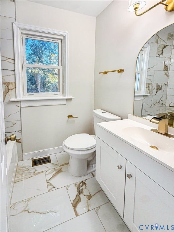 4003 Lee Boulevard, Dinwiddie, VA 23803 Bathroom featuring large-format tile flooring with gold veining, white vanity with integrated sink, brass-tone hardware and lighting, and arched mirror