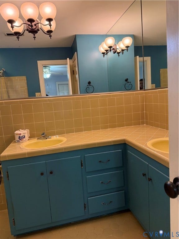 20 Jonquil Lane, Newport News, VA 23606 L-shaped vanity featuring dual integrated sinks, tile countertop, expansive wall-mounted mirror, and multi-light globe fixture