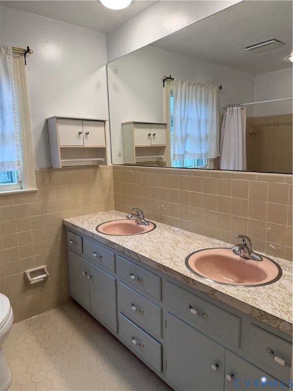 20 Jonquil Lane, Newport News, VA 23606 Dual-sink vanity featuring a patterned countertop, integrated oval basins, chrome-finish faucets, and extensive cabinetry with built-in wall storage, finished with hexagonal tile flooring and tile wall accents