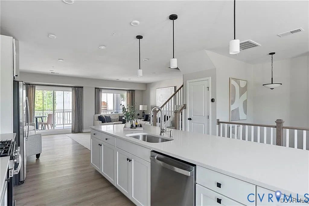 Kitchen featuring a central island with a solid surface countertop, stainless steel sink, wood-finish flooring, and pendant lighting