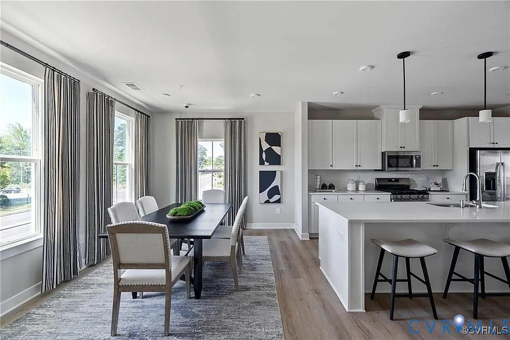 Kitchen featuring white cabinetry, an expansive center island, integrated stainless steel appliances, and wood-finish flooring