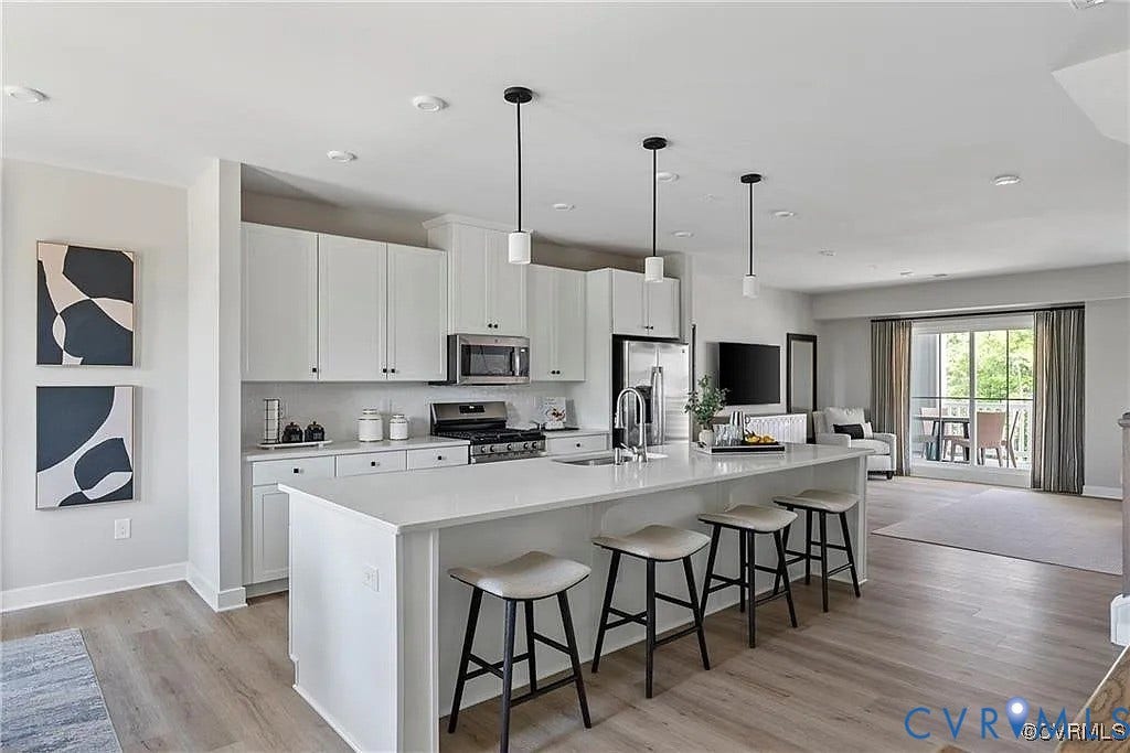 Kitchen featuring white cabinetry, an expansive central island with a solid-surface countertop, stainless steel appliances, pendant lighting, and wood-finish flooring