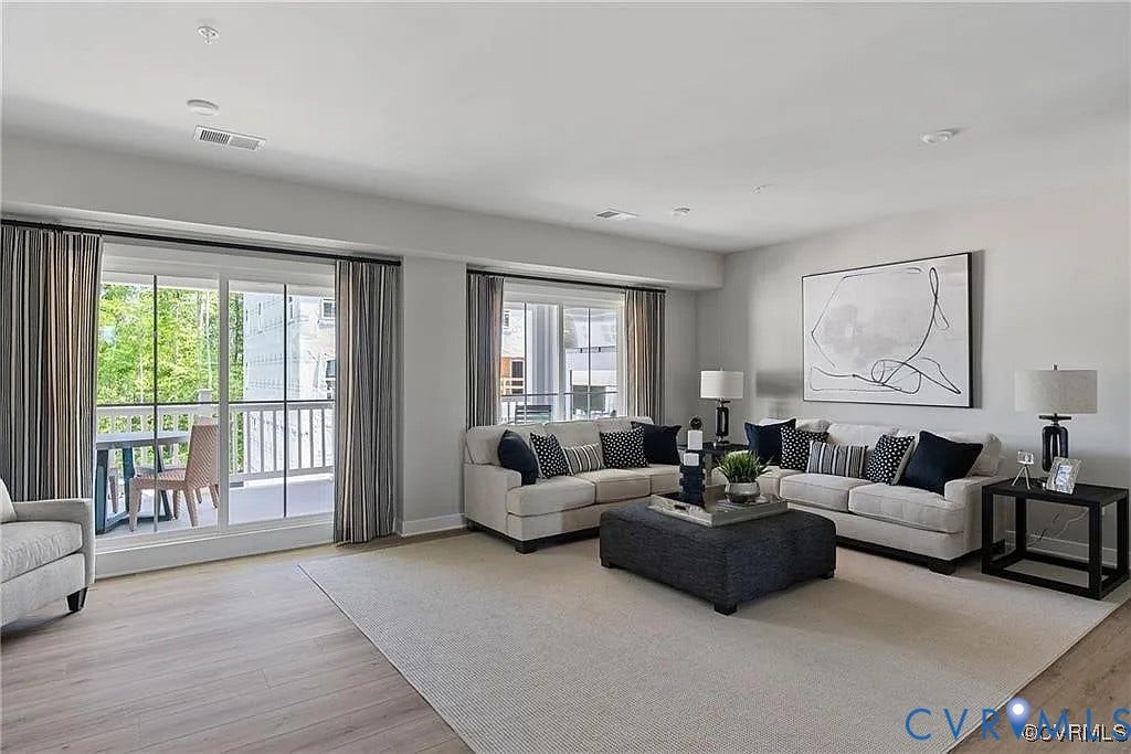 Living area featuring wood-finish flooring, neutral wall tones, large window configurations, and sliding glass doors providing outdoor access