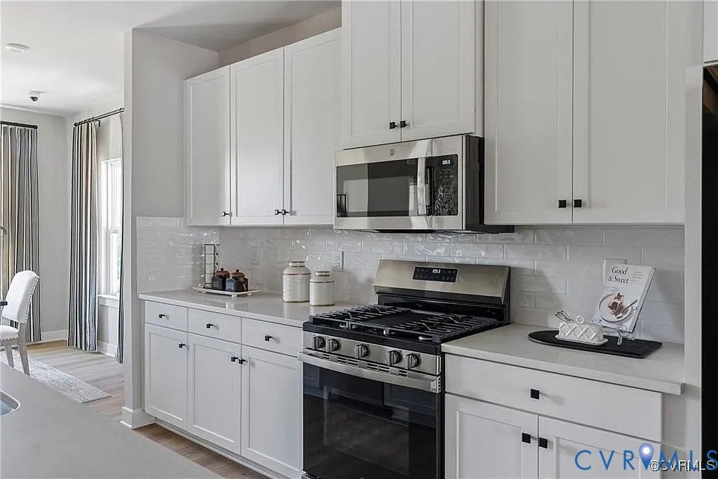 Kitchen featuring white cabinetry, subway tile backsplash, quartz countertops, stainless steel gas range, and built-in microwave