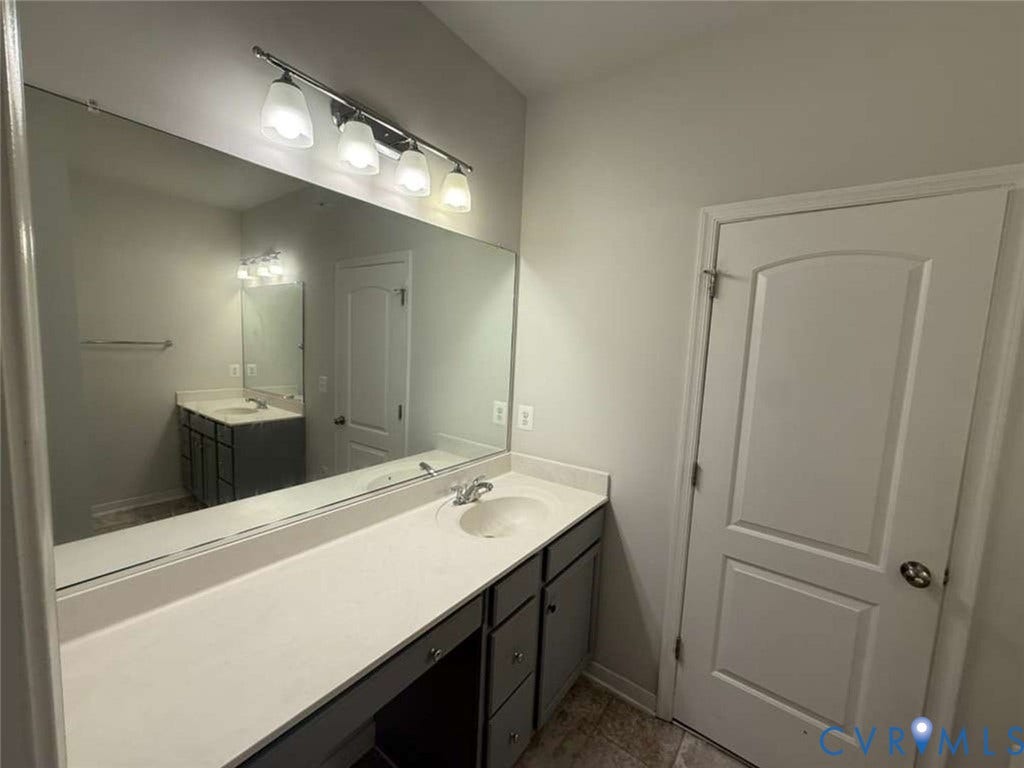 5912 Whitehurst Lane, #B, Henrico, VA 23227 Bathroom vanity featuring a solid surface countertop with an integrated basin, charcoal-finish cabinetry, a full-width wall mirror, and a four-light fixture