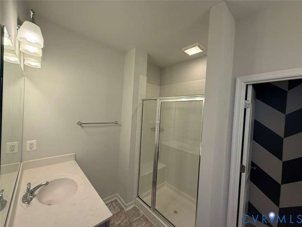 5912 Whitehurst Lane, #B, Henrico, VA 23227 Bathroom featuring a vanity with a solid-surface countertop, an integrated sink, a glass-enclosed shower with a built-in bench, and wall-mounted light fixtures