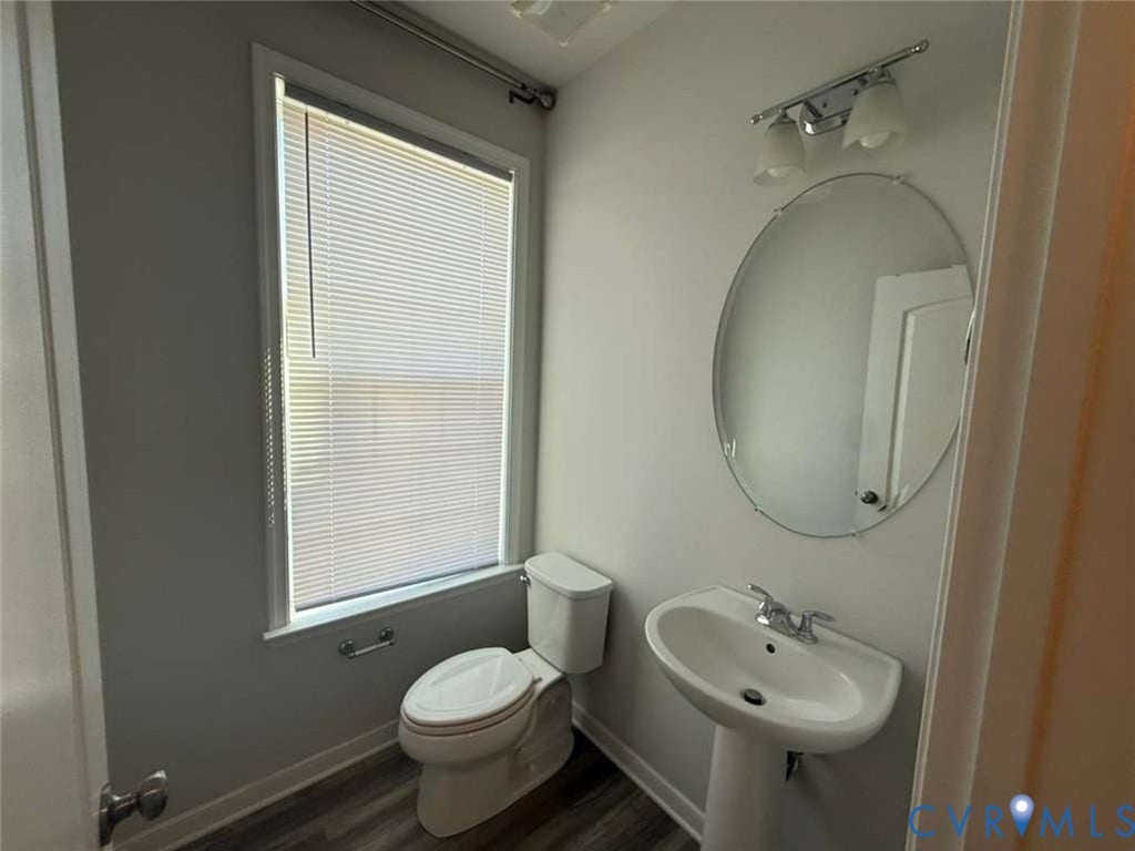5912 Whitehurst Lane, #B, Henrico, VA 23227 Powder room featuring a pedestal sink with a dual-handle faucet, oval frameless wall mirror, two-light vanity fixture, and wood-finish flooring