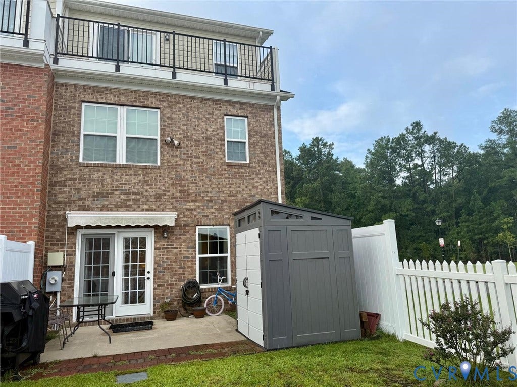 11316 Duncan park Court, Glen Allen, VA 23060 Brick exterior featuring a private concrete patio, a retractable awning, and a balcony with black metal railings, enclosed by white vinyl fencing