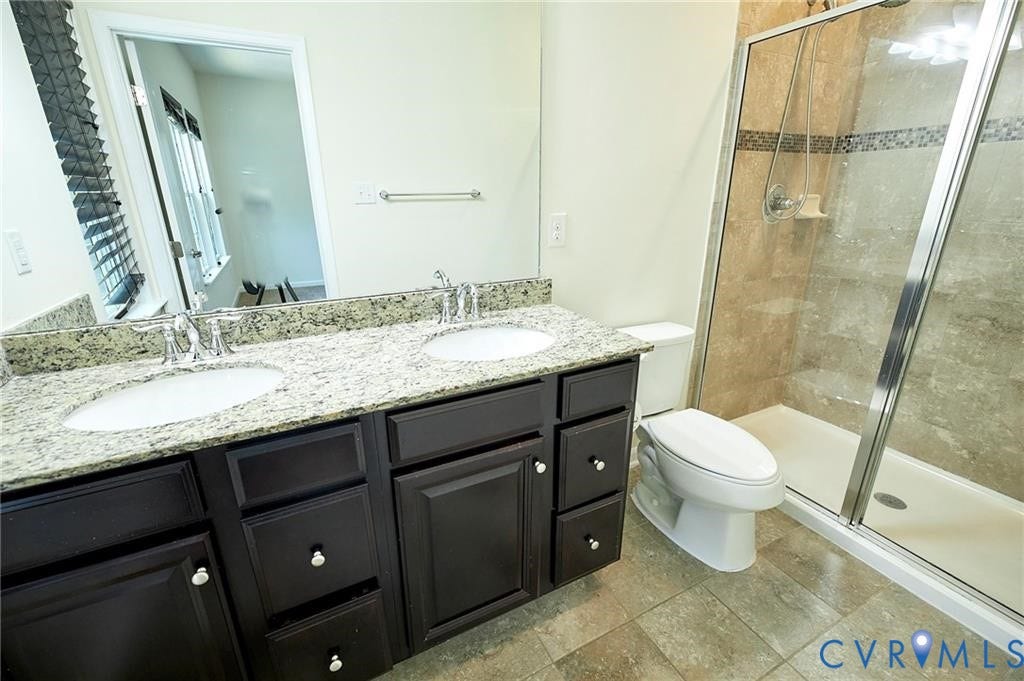 11316 Duncan park Court, Glen Allen, VA 23060 Dual-sink vanity with stone countertop and dark cabinetry, large wall-mounted mirror, and walk-in shower with stone tile surround and glass enclosure