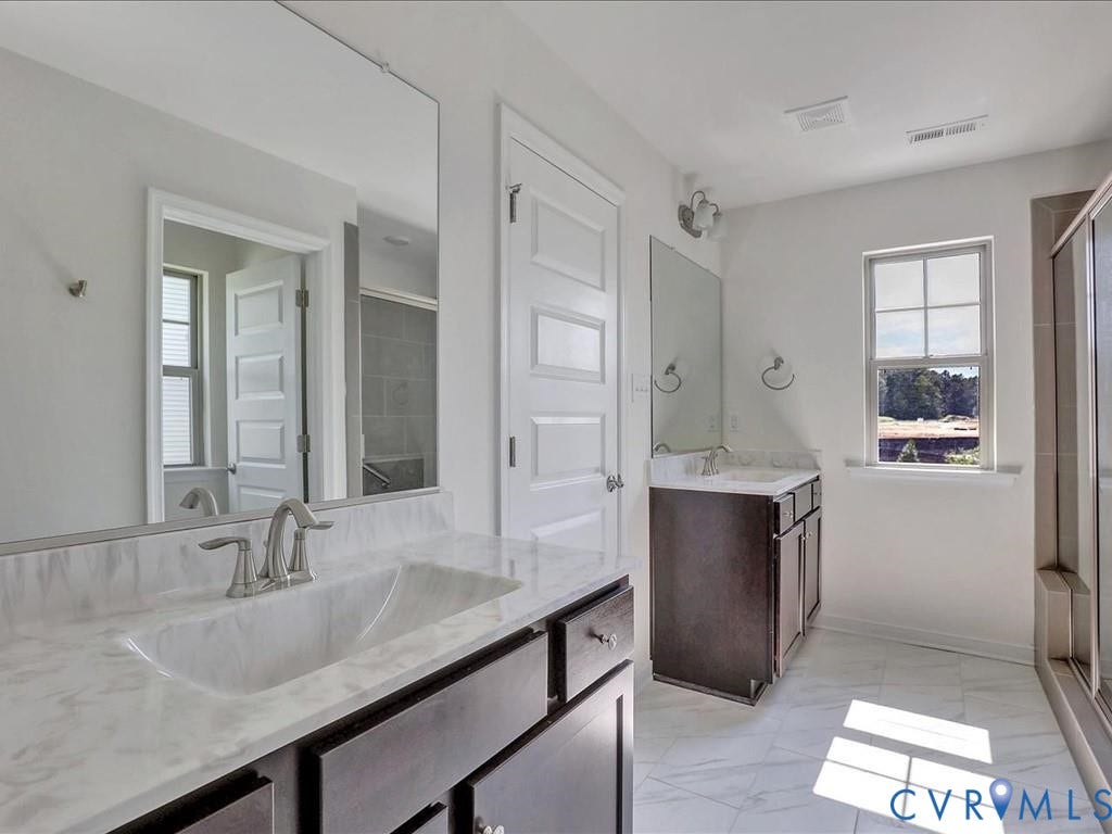 338 Hay Mill Alley, Glen Allen, VA 23060 Double vanity featuring dark cabinetry, solid-surface countertops, integrated sinks with dual-handle hardware, and expansive wall-mounted mirrors