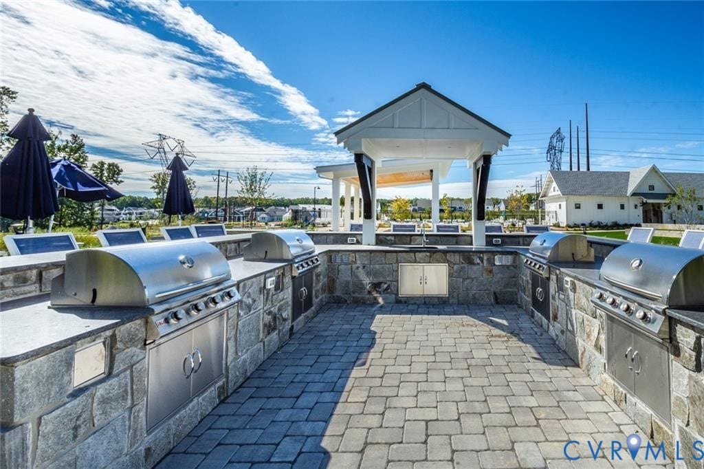 338 Hay Mill Alley, Glen Allen, VA 23060 Outdoor kitchen featuring stone masonry, stainless steel built-in grills, stone paver flooring, dark-finish countertop surfaces, and an overhead pergola structure