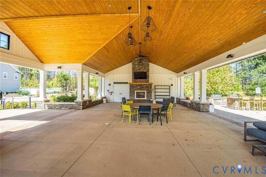 338 Hay Mill Alley, Glen Allen, VA 23060 Covered outdoor pavilion featuring a vaulted wood-plank ceiling, stone-faced fireplace with wood mantel, concrete flooring, and built-in stone masonry seating