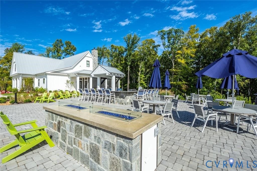 338 Hay Mill Alley, Glen Allen, VA 23060 Sprawling stone paver patio featuring a built-in outdoor kitchen with stone veneer base and concrete countertop, integrated linear fire feature, and farmhouse-style exterior architecture