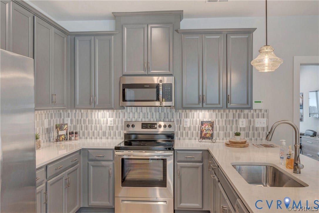Kitchen featuring gray shaker-style cabinetry, quartz countertops, a patterned tile backsplash, stainless steel appliances, and a pendant light fixture